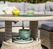 Outdoor wicker table with bowls, plates, and drink, set beside grey patio sofa for garden dining