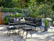 Modern black outdoor sofa set with dining table and stools on patio, surrounded by greenery