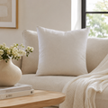 Cream linen throw pillow on luxury sofa with cozy knit blanket and vase of white flowers