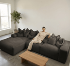 Woman in neutral lounge set sitting on modern grey sectional sofa in minimalist living room