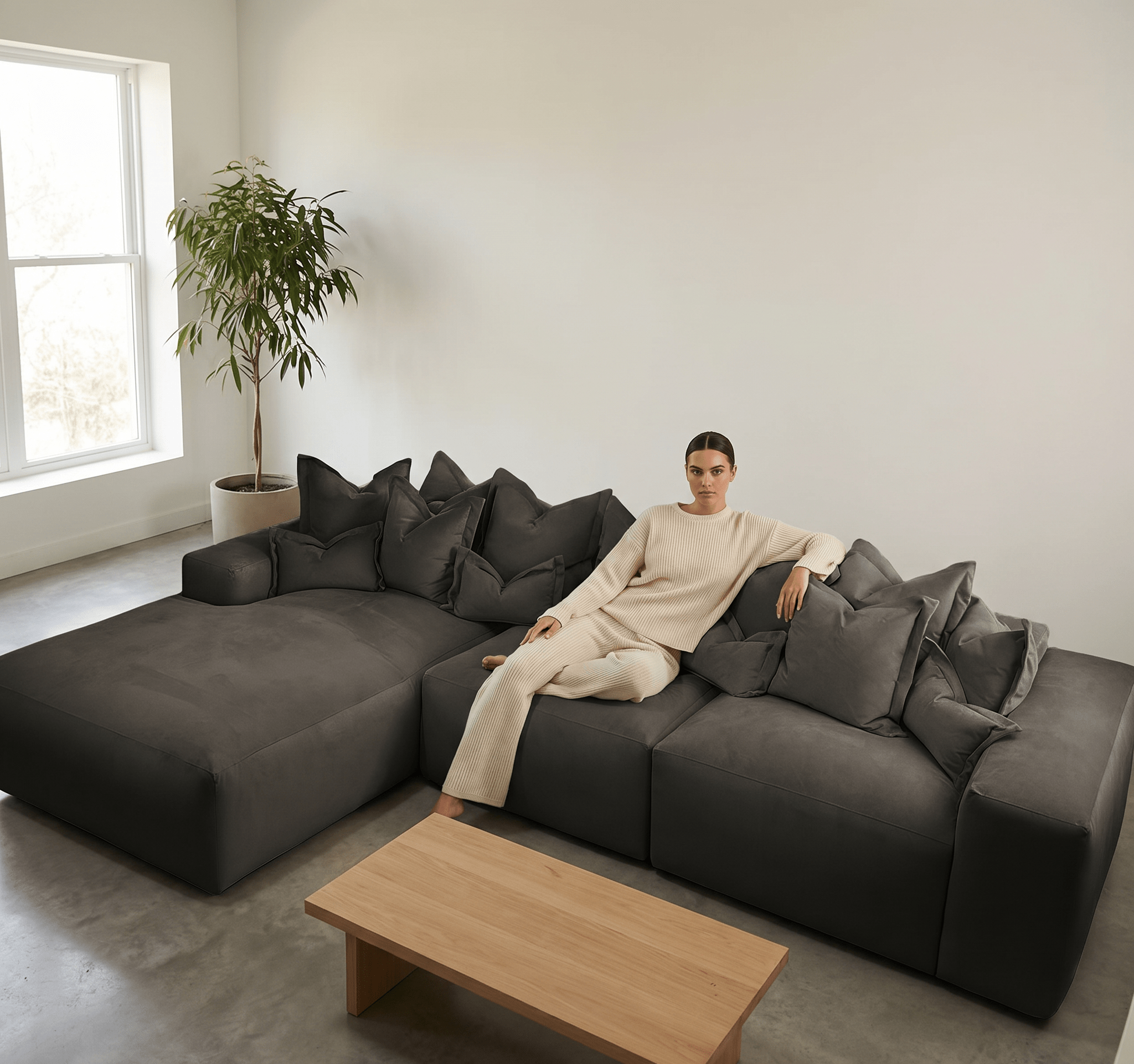Woman in neutral lounge set sitting on modern grey sectional sofa in minimalist living room