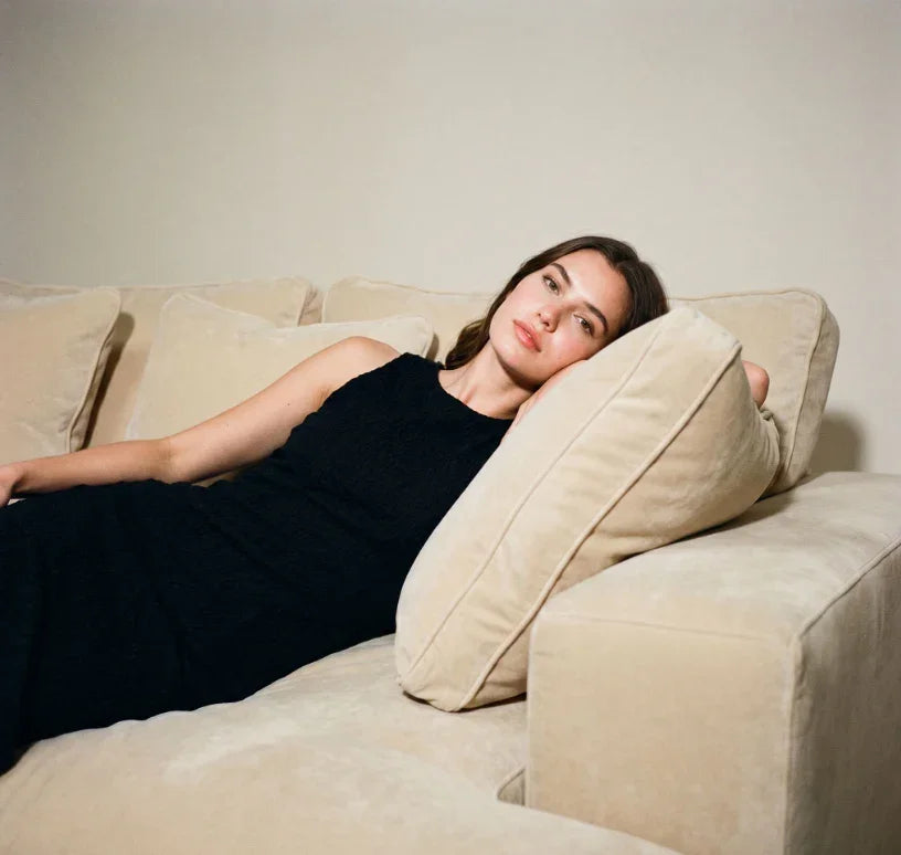 Woman in black dress reclining on beige luxury sofa, close-up of upper body and sofa texture