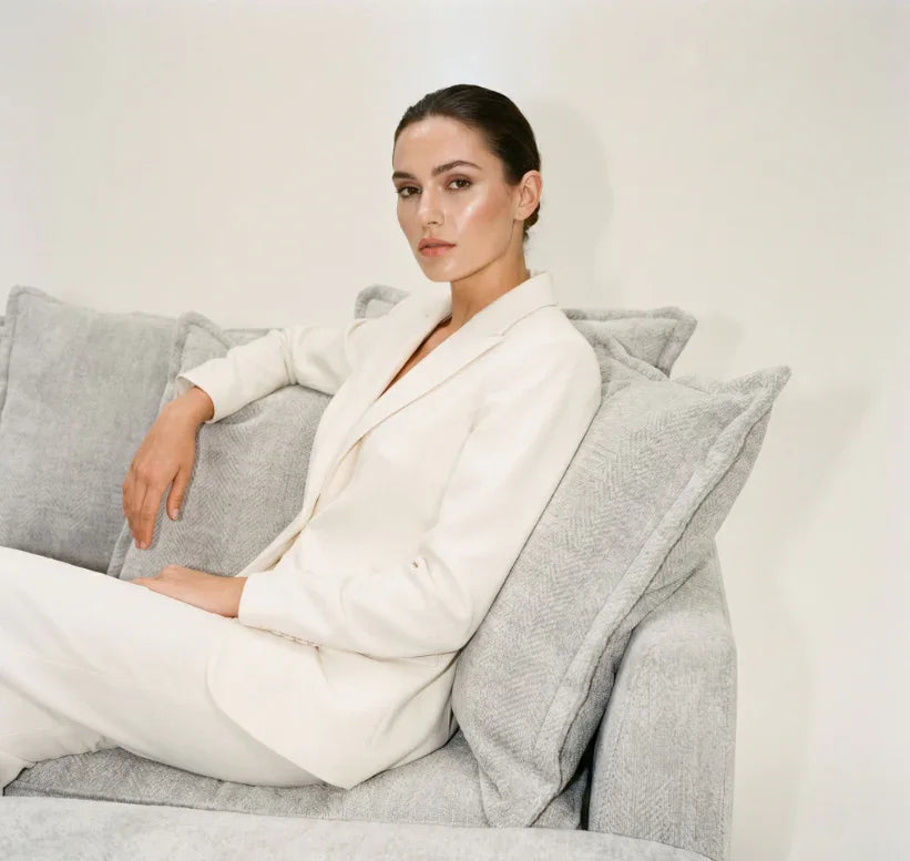 Woman in white suit sitting on a modern grey sofa with plush cushions, minimalist style
