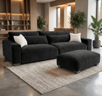 Modern black velvet sofa with matching ottoman on a textured rug in a contemporary lounge.