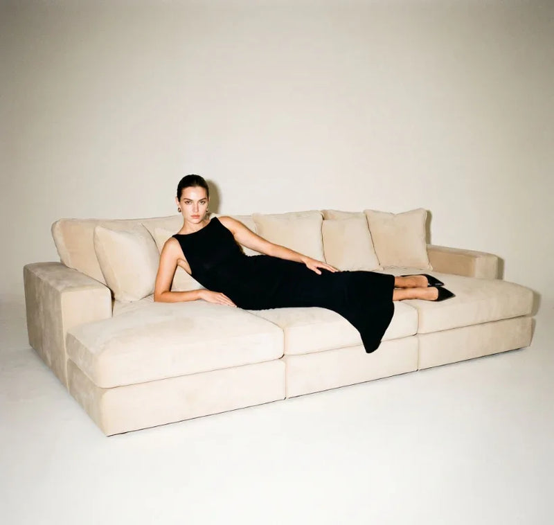 Woman in black dress lounging on large beige sectional sofa with plush cushions