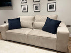 Modern beige sofa with navy cushions in a living room, wall art and wooden floor
