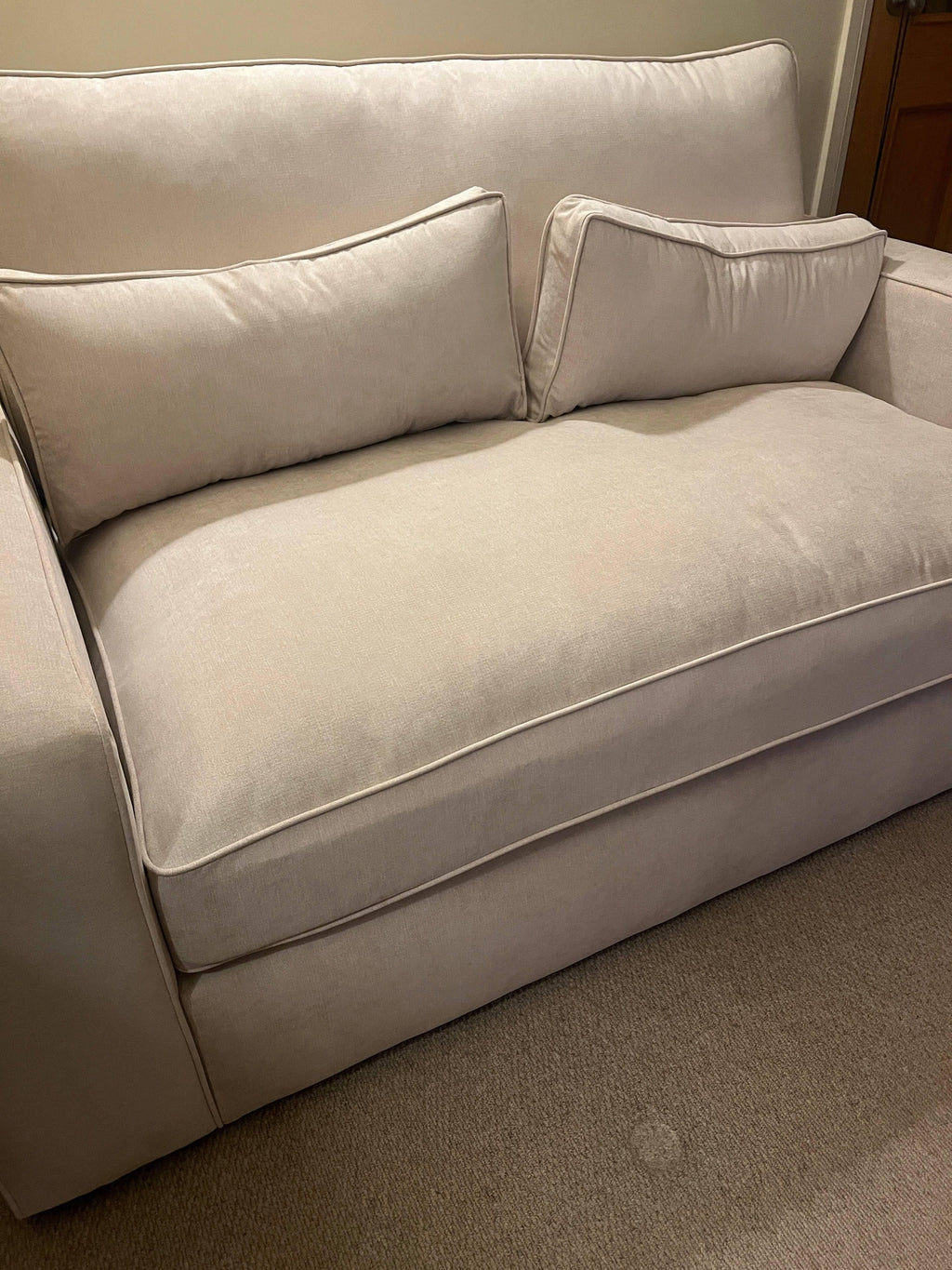 Modern beige fabric sofa with two matching cushions in a cozy living room setting