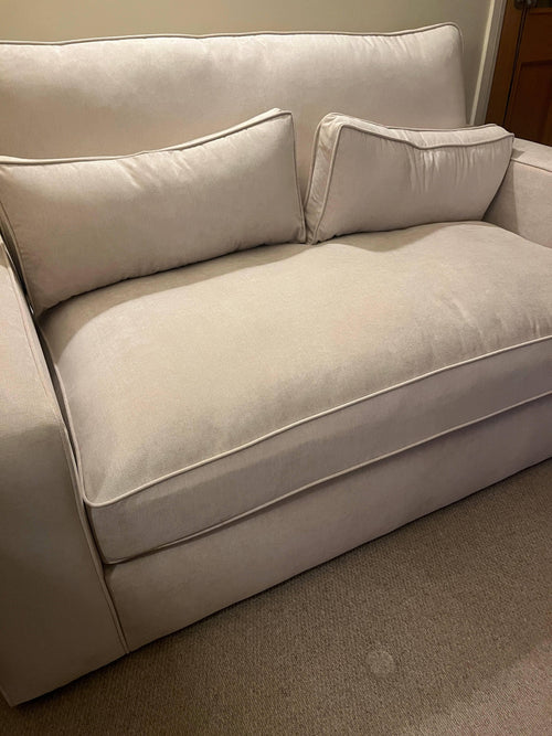 Modern beige fabric sofa with two matching cushions in a cozy living room setting