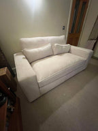 Modern cream fabric sofa with wide arms and matching cushions in a cozy living room.