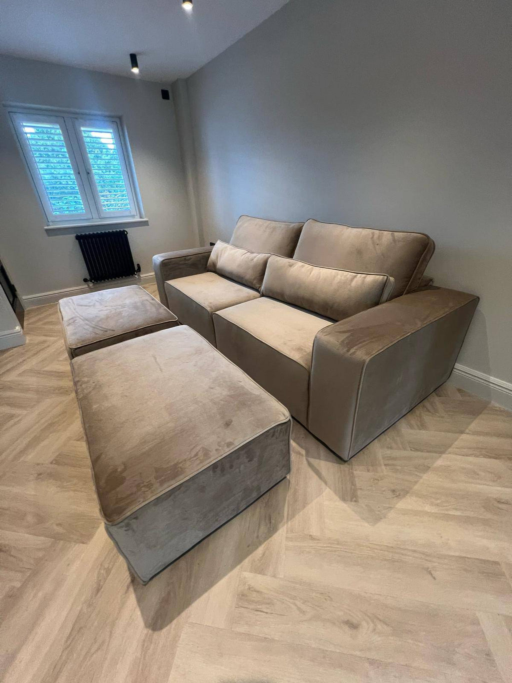 Modern beige velvet sofa with matching ottoman in bright living room with wood flooring