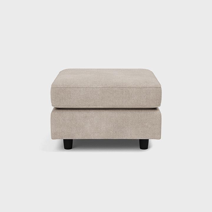 Beige upholstered footstool with black legs, minimalist design on white background