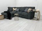 Dark grey corner sofa bed with scatter cushions in modern living room, side table and blanket