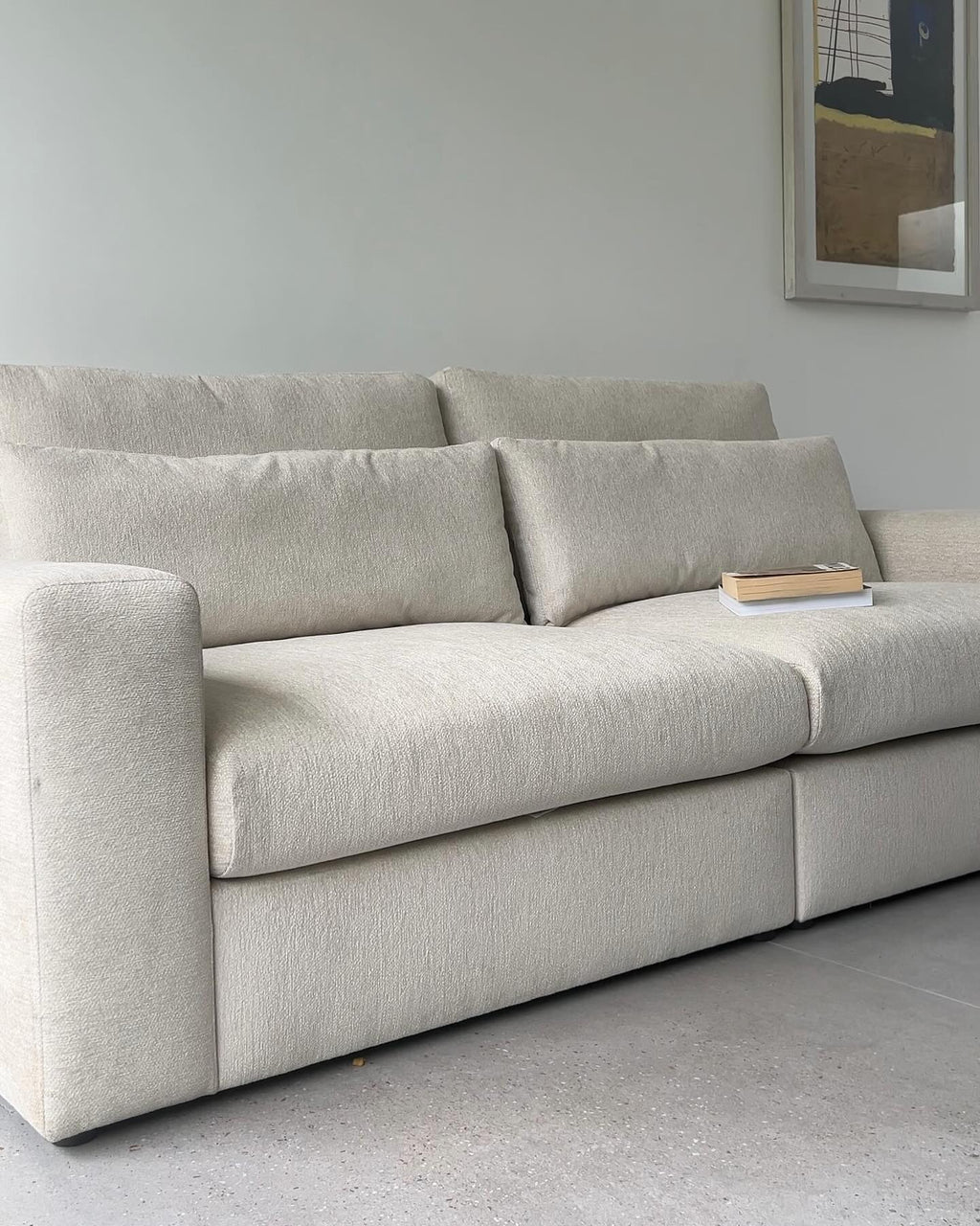 Light beige modular sofa with plush cushions in a modern living room, book on armrest.