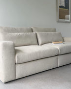 Light beige modular sofa with plush cushions in a modern living room, book on armrest.