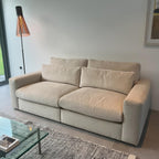 Beige modern sofa with plush cushions in a minimalist living room next to a floor lamp