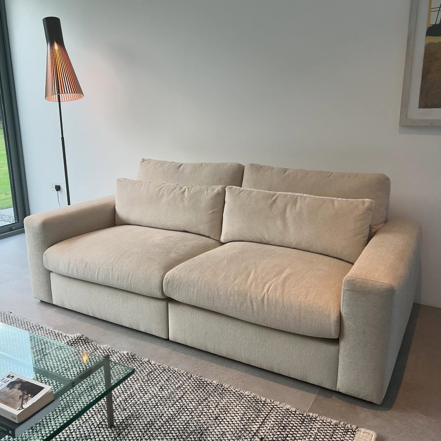 Beige modern sofa with plush cushions in a minimalist living room next to a floor lamp