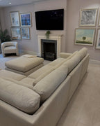 Beige modular corner sofa in modern living room with armchair, wall art, and fireplace