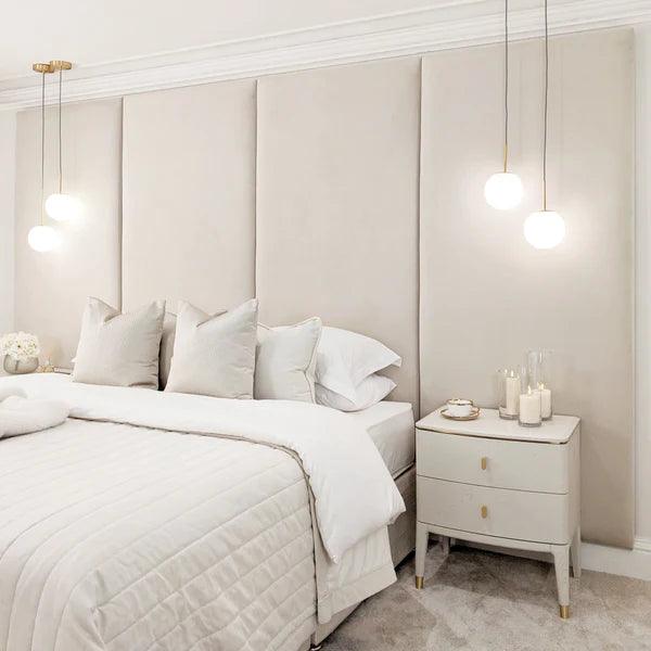 Cream velvet double bed with upholstered wall headboard panels, modern pendant lights, and bedside table.