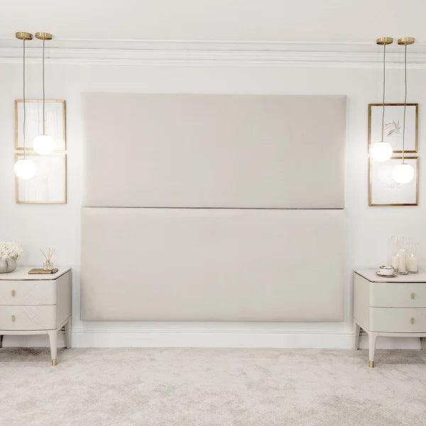 Cream velvet double-width upholstered headboard wall panel in a modern bedroom with bedside tables and pendant lights
