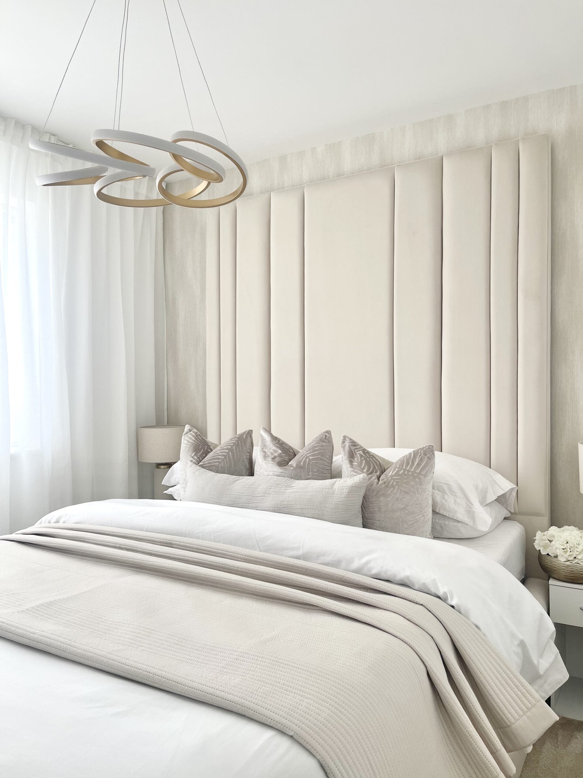 Modern double bed with tall upholstered headboard, neutral bedding, and stylish lighting