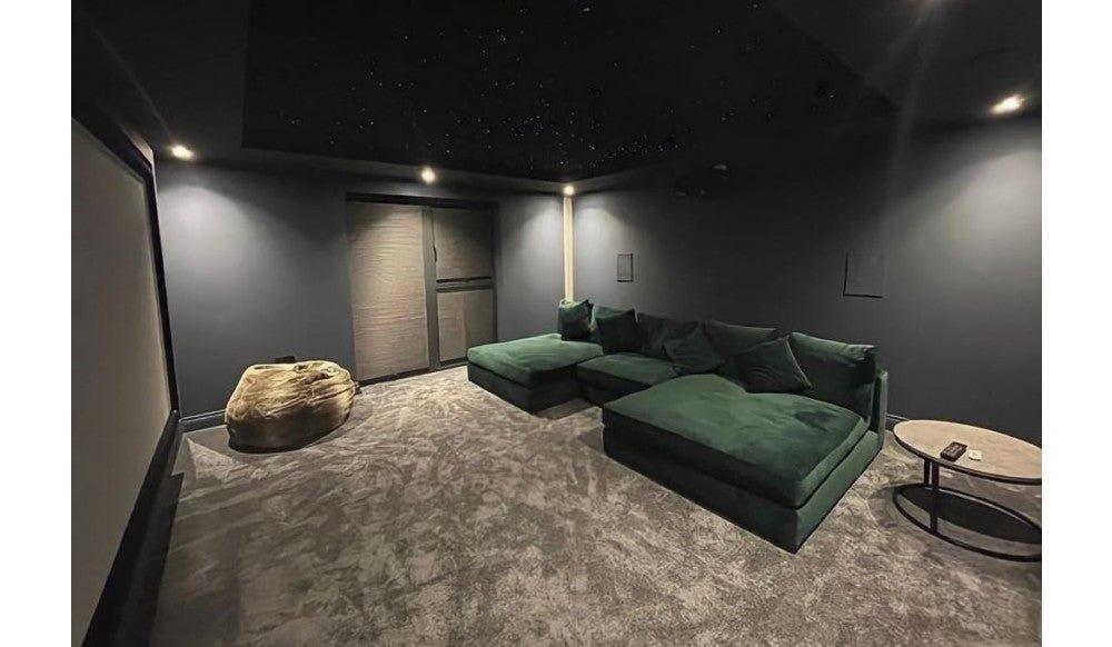 Large green cinema sofa in a modern home theater room with dark walls and plush carpet