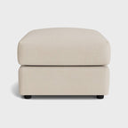 Cream fabric footstool with soft cushioning and black feet on a white background