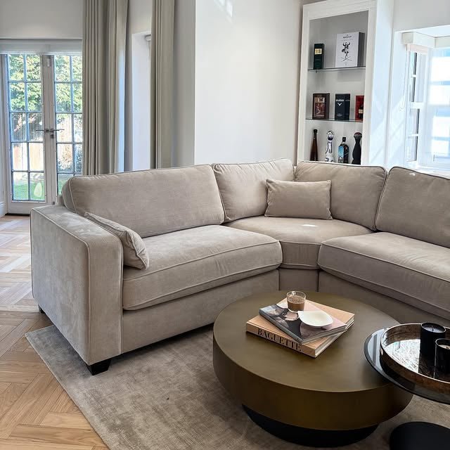 Modern beige corner sofa in a bright living room with round coffee table and books.