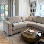 Modern beige corner sofa in a bright living room with round coffee table and books.