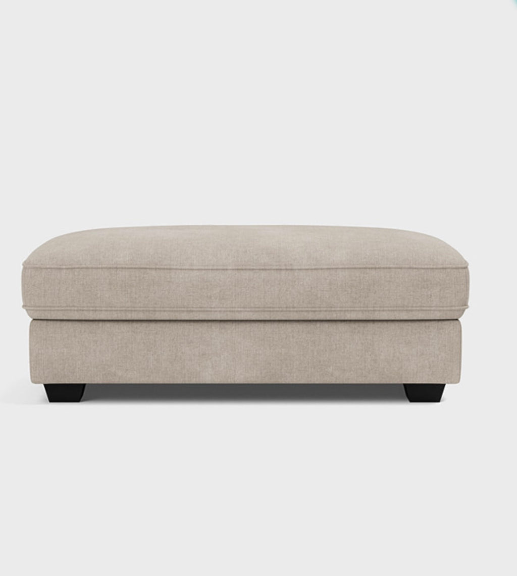Modern beige fabric ottoman with low black legs on a white background