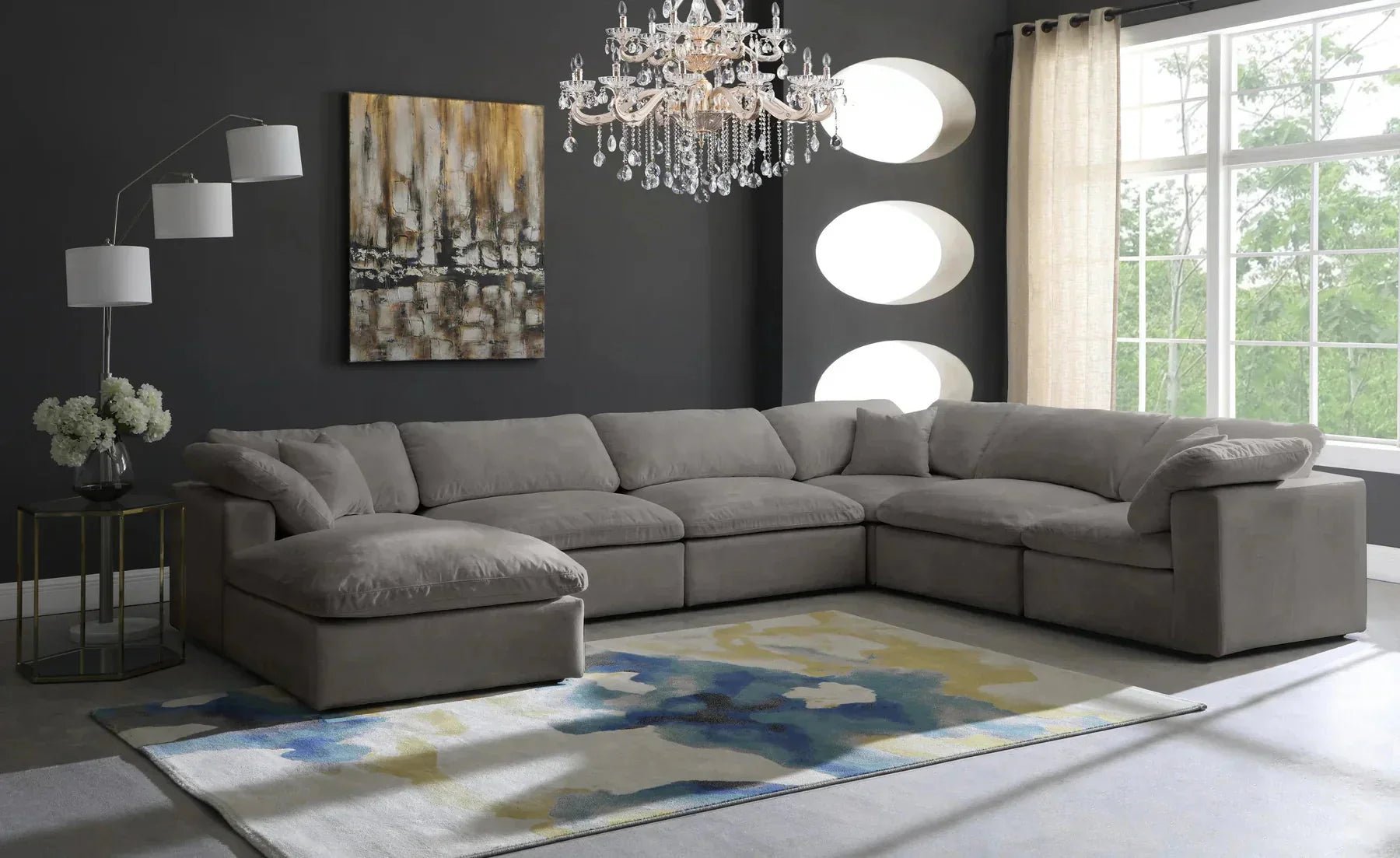 Modern living room with large cream modular corner sofa, ottoman, chandelier, and abstract rug