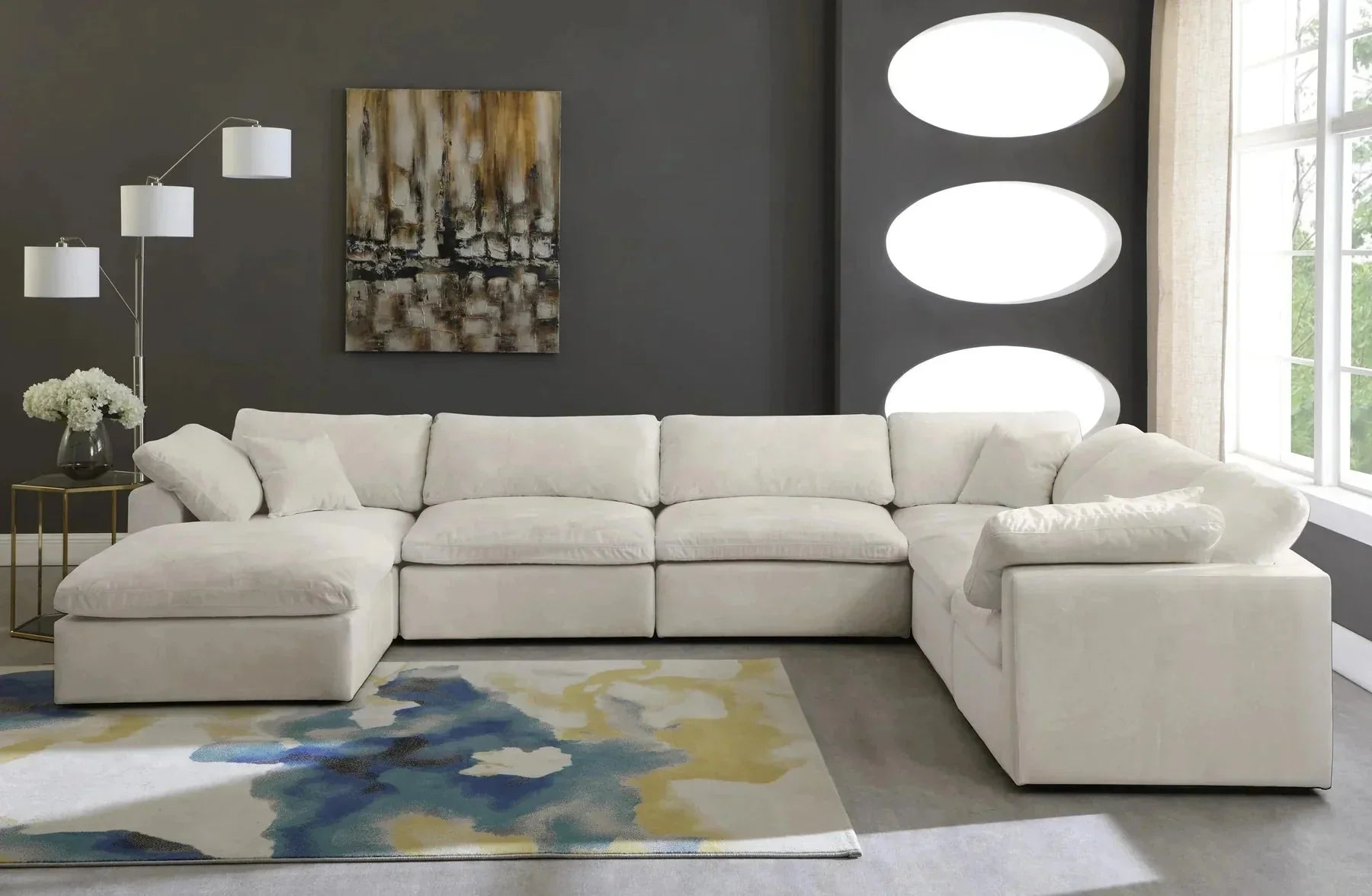Cream modular corner sofa with footstool in modern living room, abstract rug, and wall art.