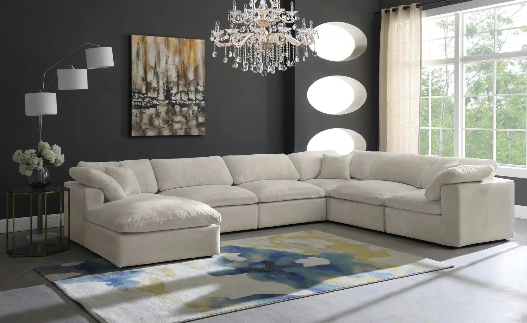 Cream modular corner sofa with footstool in modern living room with chandelier and abstract art