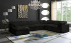Modern living room with large black modular corner sofa, abstract rug, chandelier, and wall art.