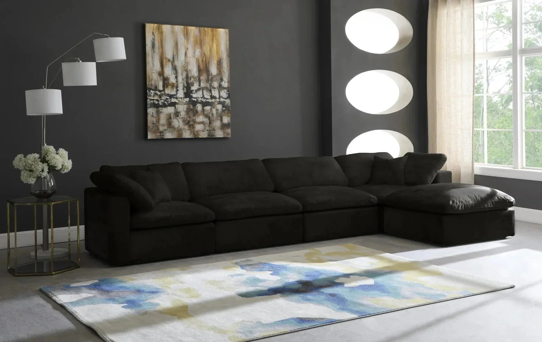 Modern living room with black modular corner sofa, abstract rug, floor lamp, and wall art.