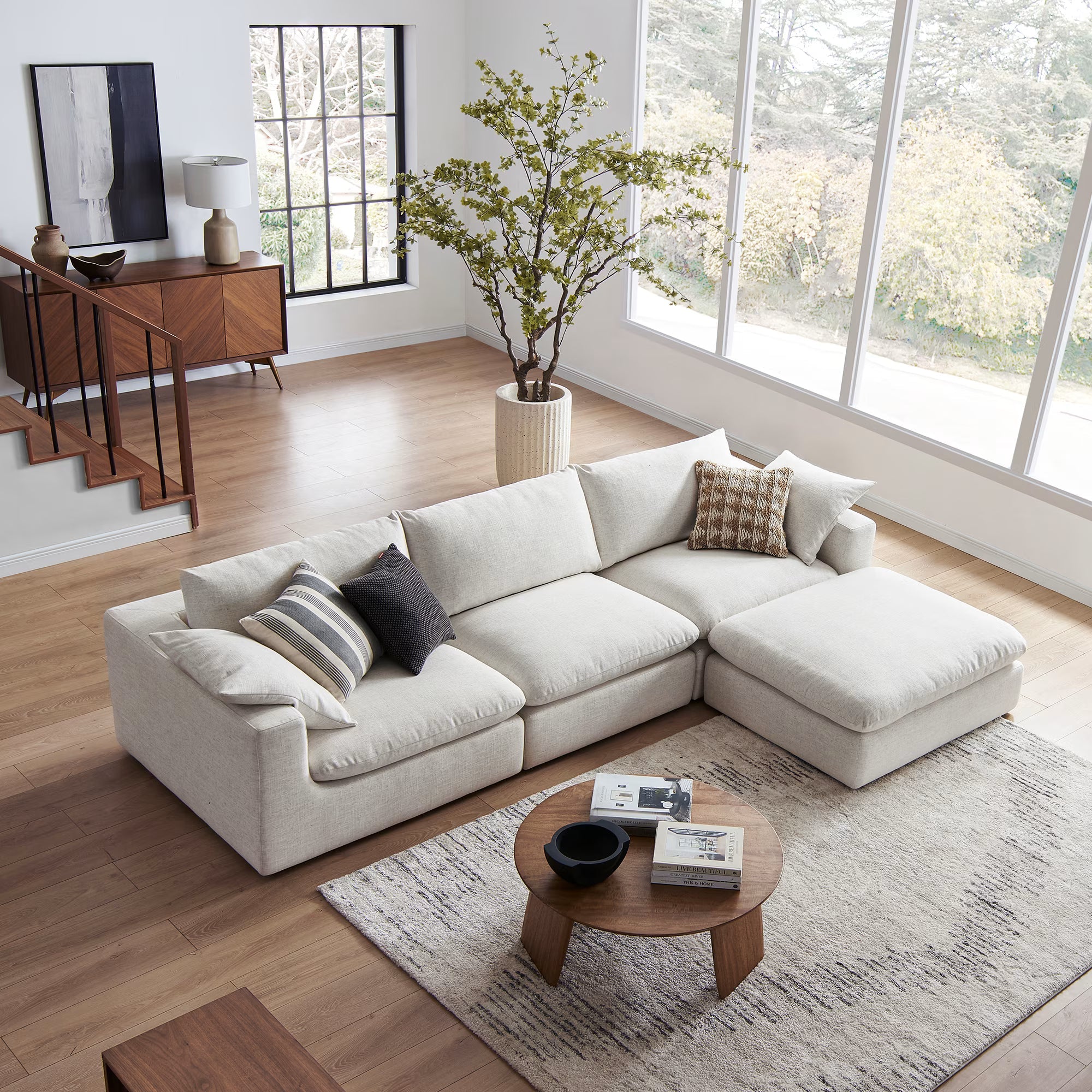 Modern cream modular sofa with footstool in bright living room, wood floors, and large windows