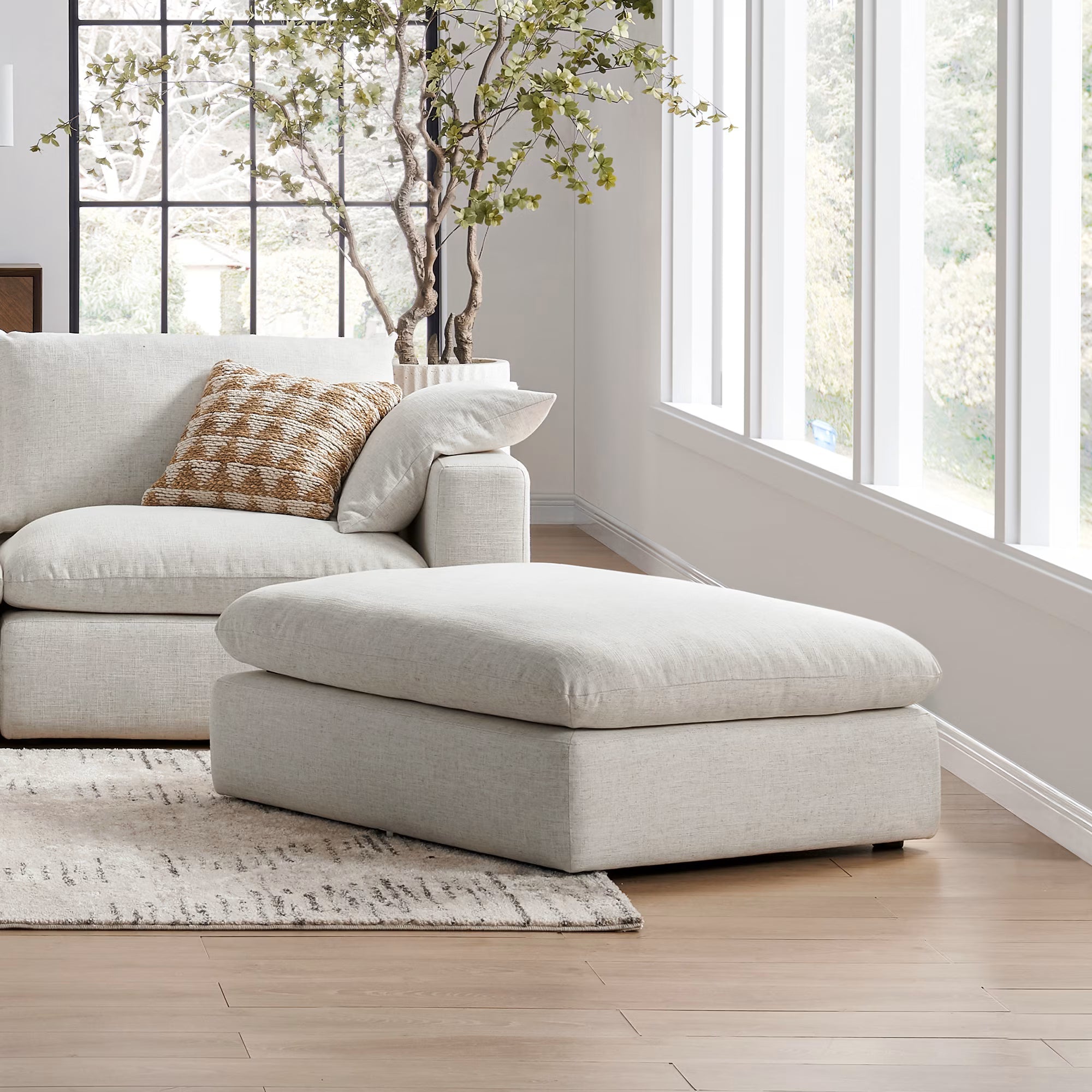 Cream modular footstool and sofa in a bright modern living room with large windows.