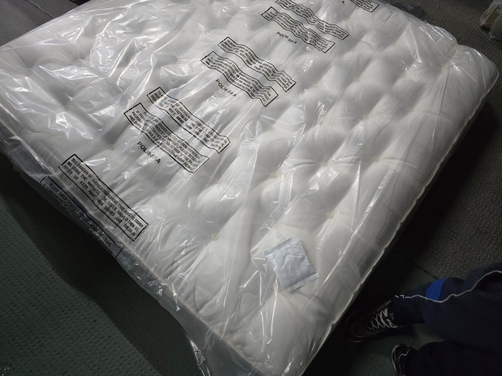 Emperor size, tufted white mattress wrapped in protective plastic on carpeted floor