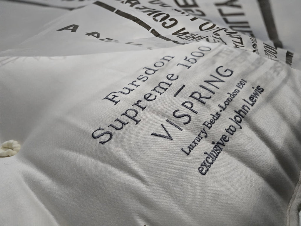 Close-up of Vispring luxury mattress with embroidered label and tufted cotton fabric.