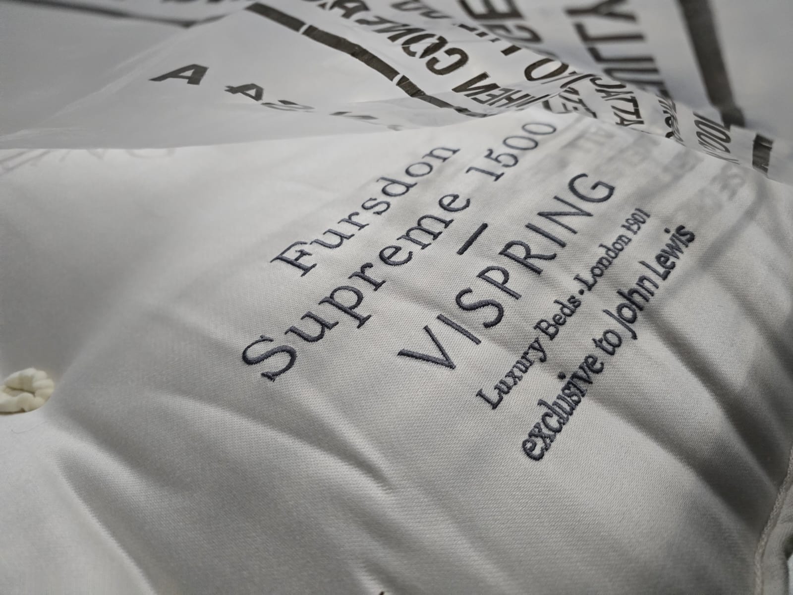 Close-up of Vispring luxury mattress with embroidered label and tufted cotton fabric.
