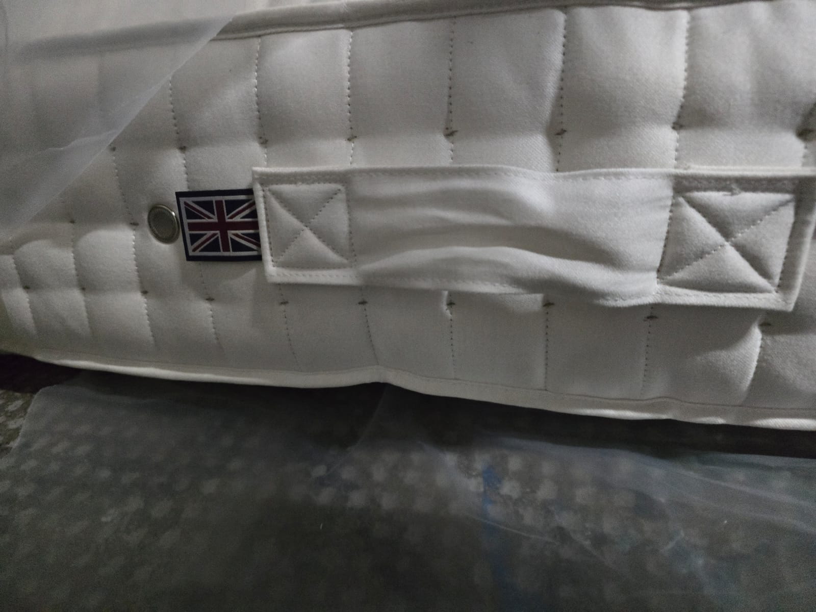 Close-up of luxury white mattress with quilted pattern, fabric handle, and UK flag label