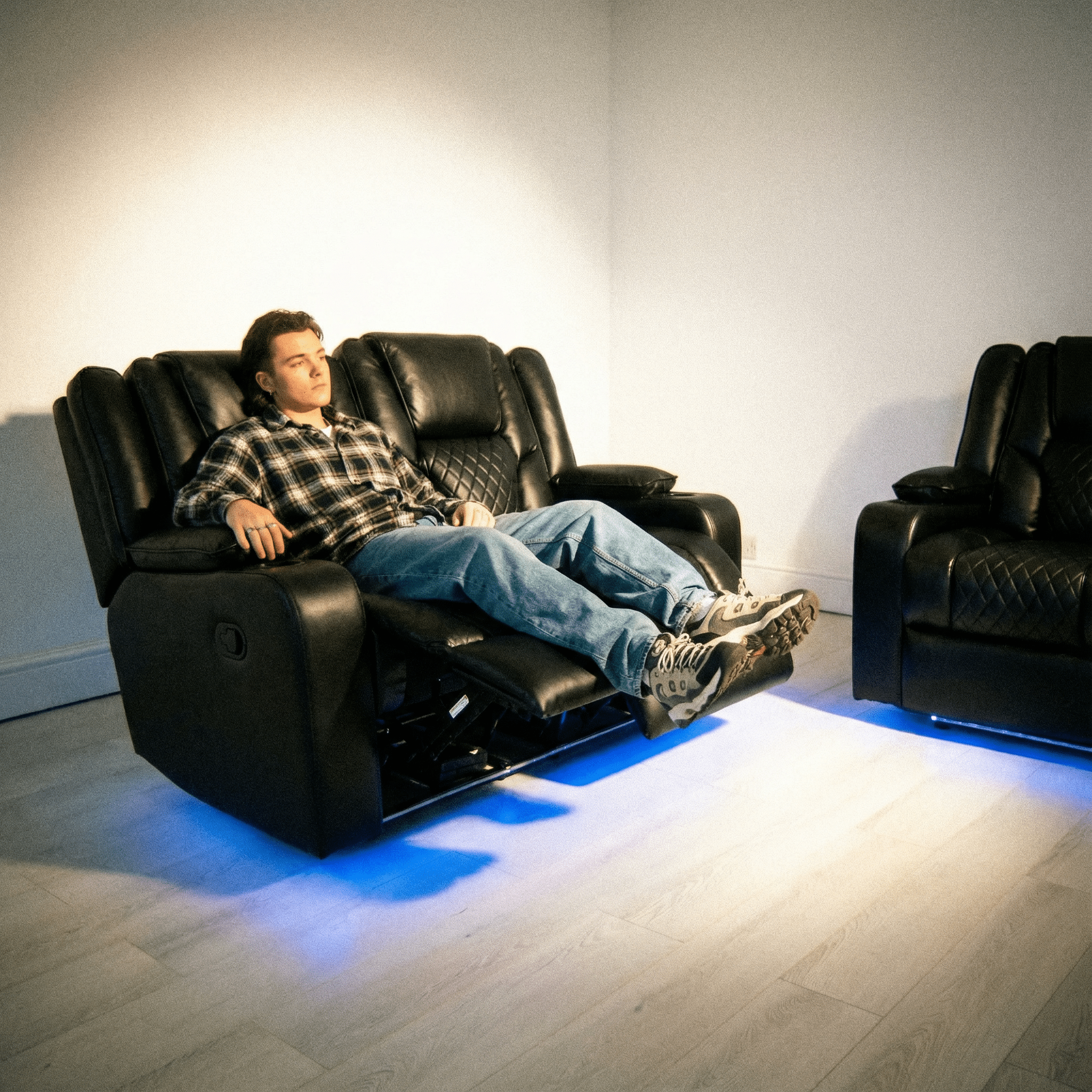 Modern black leather electric recliner sofa set with blue LED lighting and a person relaxing