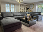 Grey modular corner sofa in a modern living room with large wall clock and glass coffee table.