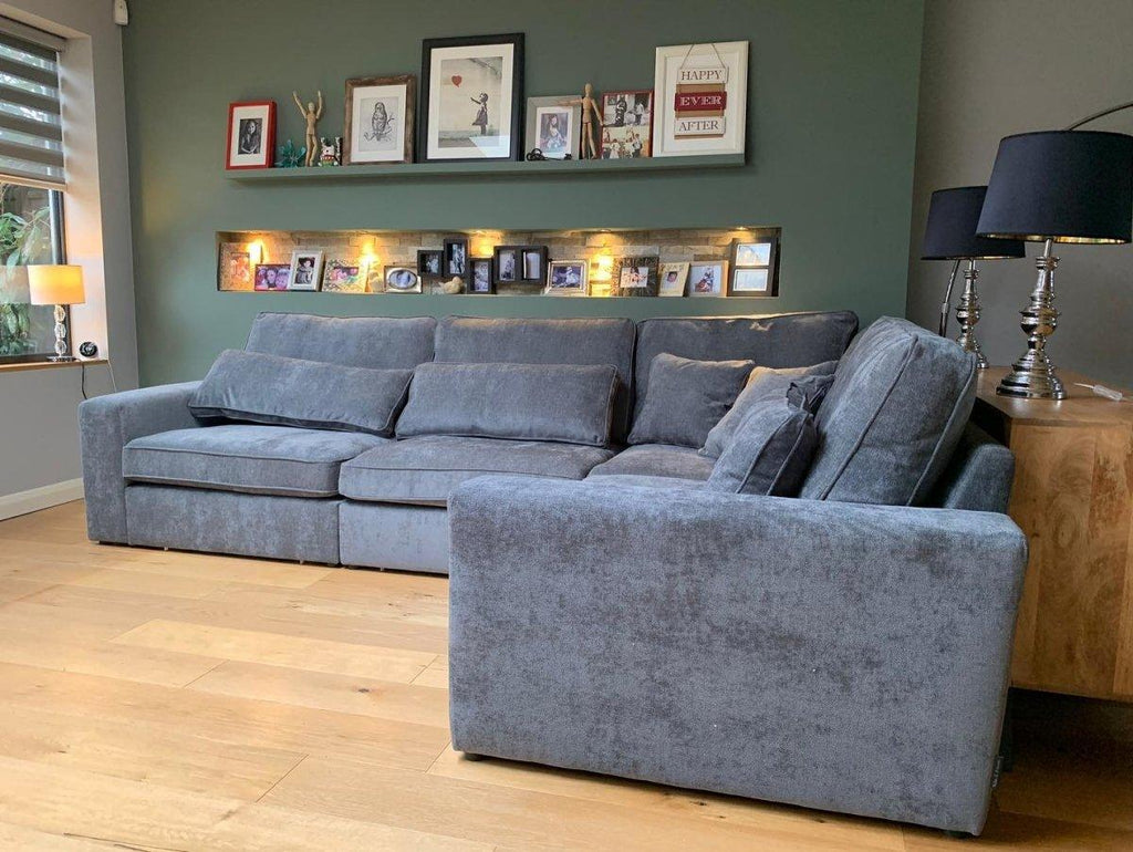 Grey modular corner sofa in modern living room with wooden floor and wall shelves.