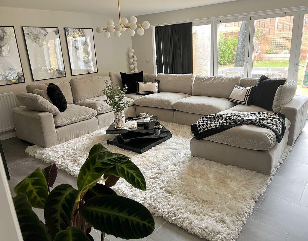 Large U-shaped beige modular sofa with footstool in modern living room, on plush white rug.