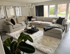 Large U-shaped beige modular sofa with footstool in modern living room, on plush white rug.