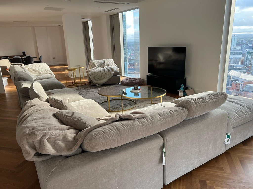 Large U-shaped modular sofa with footstool in modern living room, city view windows, gold coffee tables
