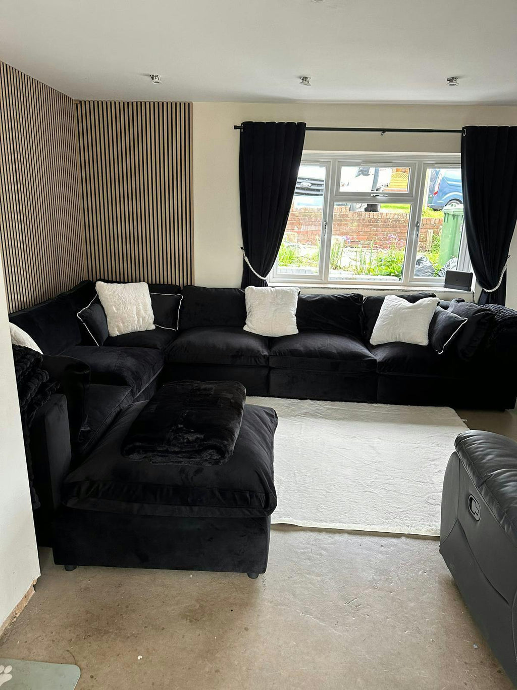 Modern living room with large black U-shaped modular sofa, matching footstool, and white cushions