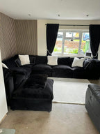 Modern living room with large black U-shaped modular sofa, matching footstool, and white cushions