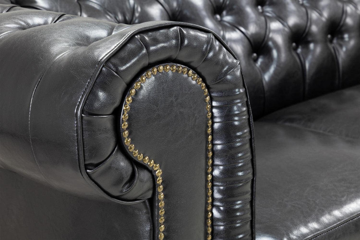 Close-up of black leather Chesterfield sofa arm with tufted back and brass stud details