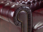 Close-up of oxblood red Chesterfield leather sofa arm with tufted design and brass studs